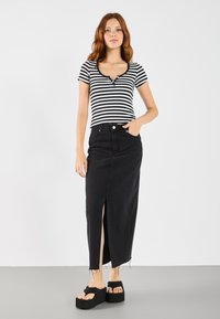 Svart denim maxiskjørt med frontslitt, kombinert med en svart og hvit stripete topp med korte ermer, rund hals og knapper.
