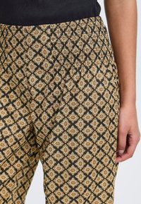 Pantalons noirs à motif avec un motif de losanges floraux répétés en or et beige, dotés d'une taille élastique froncée pour plus de confort.