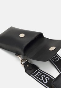 Sort læder crossbody taske med trykknaplukning, der har en struktureret overflade og en kontrasterende mønstret rem.