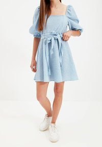 Krátký rukáv, šaty s čtvercovým výstřihem v světle modré barvě s kostkovaným vzorem, stahovaný v pase a s páskem ze stejné látky. V kombinaci s bílými teniskami.