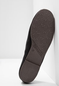 Chaussure plate noire reposant sur le côté, montrant la semelle avec un motif de bande de roulement texturé, la marque Tamaris et la taille 37.