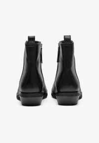 Botas de tobillo de cuero negro con una textura suave, puntera afilada, cremalleras laterales y un tacón bajo tipo bloque para mayor estabilidad. Detalles de costura reforzada.
