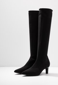 Bottes noires hautes jusqu'au genou en tissu lisse avec un bout pointu et un talon effilé modeste, présentant des coutures verticales nettes.