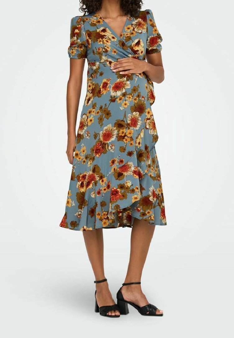 Femme portant une robe cache-cœur bleue à motifs floraux avec des manches courtes bouffantes et des sandales noires à talons blocs avec bride cheville, debout avec une main sur la taille.