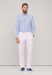 Camicia a righe blu e bianca con bottoni abbinata a pantaloni rosa chiaro e sneakers blu, caratterizzata da una texture liscia e una vestibilità sartoriale.
