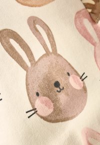 Bavlněná látka s hnědým obličejem králíčka, růžovými tvářičkami a detaily uší, na krémovém pozadí. Měkká textura s potiskem vzorů.