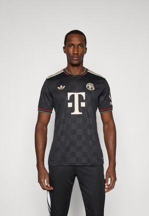 Sort kortærmet jersey med ternet mønster, hvide accenter og et stort centralt logo. Har grønne og røde kantbånd på kraven og ærmerne.