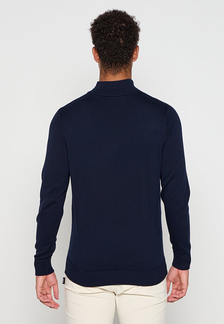 Pull en maille bleu marine avec un col montant, des manches longues, des poignets et un ourlet côtelés. Texture lisse, design minimaliste, sans motifs visibles.