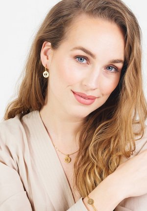 Gouden sieradenset met een ronde ketting met hanger, een bijpassende armband en kleine creolen met een letterdetail. Levendige, glanzende afwerking.