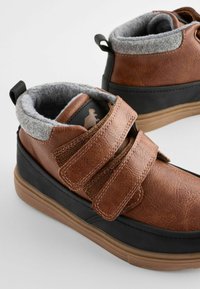 Bruine leren hoge schoenen met grijze fleece voering, zwarte rubberen zolen en twee klittenbandsluitingen voor een veilige bevestiging.