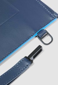 Carpeta de cuero azul marino con una textura suave, interior azul brillante en contraste y un clip de metal negro para un cierre seguro.