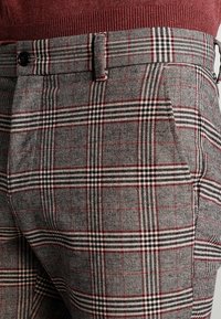 Szare spodnie w kratę z wzorem w kratkę z czerwonymi i czarnymi liniami, o flanelowej fakturze, z płaskim przodem i bocznymi kieszeniami.