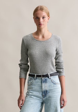 Maglione grigio a maniche lunghe con scollatura rotonda, abbinato a jeans azzurri a vita alta, con una cintura nera e fibbia argentata.