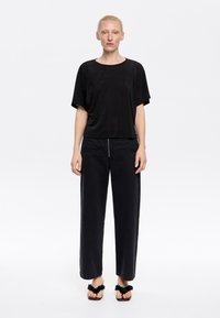 Top nero a maniche corte con una vestibilità rilassata, abbinato a pantaloni neri a gamba larga con una cerniera centrale, completato da sandali neri con accenti testurizzati.