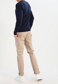 Marineblauwe gebreide trui gecombineerd met beige taps toelopende broek en witte sneakers. De outfit heeft een slim-fit ontwerp, geribbelde manchetten en opgerolde broekspijpen.