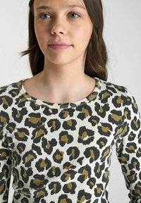 Langemouwenshirt met een witte basis en een geribbelde textuur, bedrukt met een overal olijfgroene en zwarte luipaardprint.