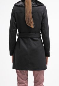 Svart ullkappa med krage i faux päls, bälte vid midjan och medellång design. Slät textur och skräddarsydd passform.