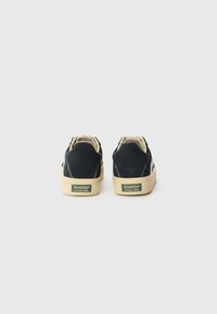 Baskets en suede noir avec des semelles en caoutchouc beige et des coutures contrastées. Présente un patch logo vert sur le talon.