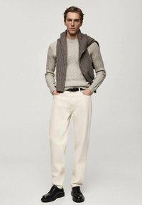 Helles grauer Kabelstrickpullover, kombiniert mit einem dunkelgrauen Schal, dazu off-white Hosen und schwarze Schnürschuhe. Schlicher, moderner Stil.