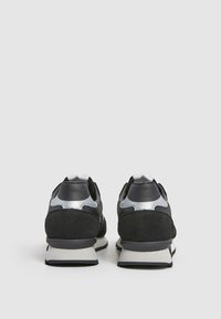 Black athletic shoes feature a combination of suede and mesh materials, a silver accent at the heel, and a white midsole.