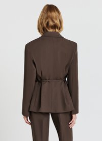 Blazer marrone su misura con design peplum, dotato di una fessura sul retro e una cintura da annodare. Texture liscia e vestibilità strutturata.