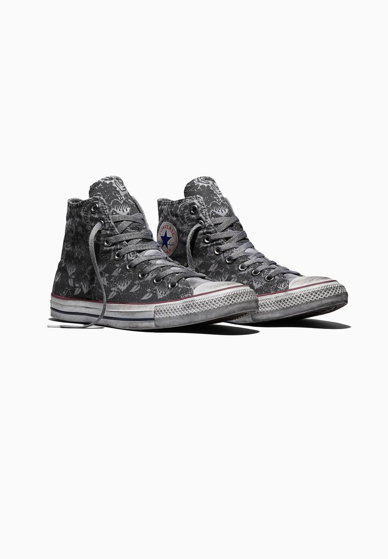 Scarpe da ginnastica Converse alte grigie usurate con motivo floreale nero, punte in gomma bianca e lacci, posate affiancate su sfondo bianco.