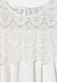 Vestido blanco con una parte superior de encaje que presenta intrincados patrones florales y bordes ondulados, fabricado con un tejido suave y una sección inferior plisada.