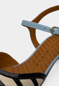 Μαύρο και μπεζ σανδάλι με λουράκια και φωτεινό γαλάζιο λουράκι στον αστράγαλο, με λεία υφή και επίπεδη, καφέ σόλα με ανάγλυφες γραμμές.