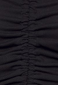 Tessuto nero con una prominente texture arricciata, caratterizzato da pieghe orizzontali. Il materiale appare morbido con una fine rigatura su tutta la superficie.