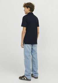 Marinblå polo med krage, korta ärmar och sidofickor, tillsammans med ljusblå slitna jeans och mörka skor med vita accenter.