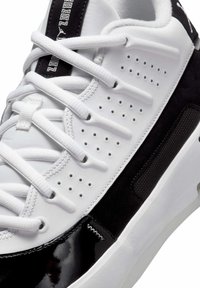 Hvide sneakers med sorte suede detaljer og blanke sorte accenter. Har perforeret design, flade hvide snørebånd og en tekstureret gummisål.