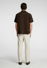 Camicetta marrone a maniche corte realizzata in un tessuto leggero, abbinata a pantaloni in lino beige, con una vestibilità rilassata e un design a gamba dritta.