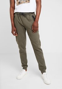 Olijfgroene joggers van zachte katoen, met een elastische tailleband met trekkoord, zijzakken met rits en geribbelde boorden.