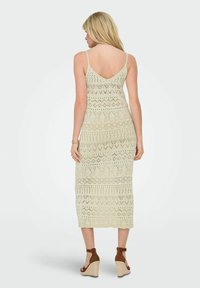 Rochie de croșetat crem, până la genunchi, cu decolteu în V, bretele subțiri și modele intricate. Asortată cu sandale cu toc wedge maro.