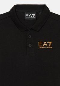 Czarna koszulka polo z kołnierzykiem, z trzema czarnymi guzikami. Złoty haftowany logo "EA7 EMPORIO ARMANI" po lewej stronie. Miękka bawełniana tekstura.