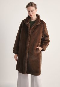 Brązowy płaszcz ze sztucznego futra z szerokim kołnierzem, długimi rękawami i bocznymi kieszeniami, charakteryzujący się miękką fakturą i luźnym, oversize'owym krojem.