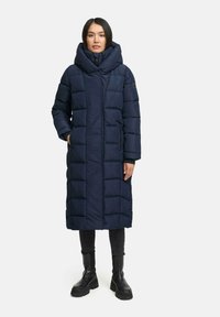Palton lung puffer de culoare bleumarin, cu glugă mare, textură matlasată, fermoar în față și buzunare laterale. Fabricat din material durabil și rezistent la apă.