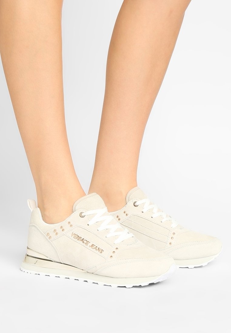 Baskets en daim beige clair avec semelle blanche, lacets à l'avant, accents embellis et logo sur le côté.