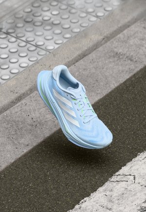 Hellblauer Laufschuh mit strukturiertem Obermaterial, weißen Streifen und grünen Akzenten. Für Leistung konzipiert, mit einer gepolsterten Sohle.