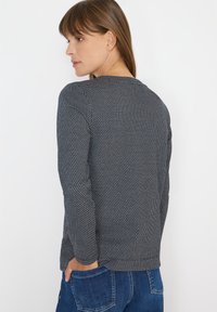 Schwarz-weiß gemusterter Langarmshirt mit rundem Ausschnitt, von hinten gezeigt, kombiniert mit blauen Jeans.