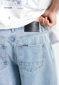 Jasnoniebieskie dżinsy z denimu z czarną skórzaną metką w talii. Posiadają pięć kieszeni, metalowe akcesoria oraz teksturowane wykończenie.