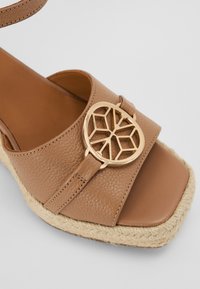 Sandale espadrille en cuir tan avec un bout carré, dotée d'un accent géométrique en or sur la lanière et d'une semelle en jute tressé.