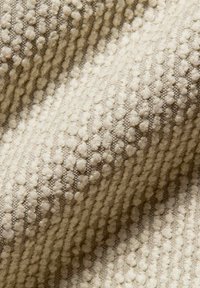 Tessuto crema con texture a rilievo, caratterizzato da piccole palline disposte in file diagonali su una base a trama fitta.