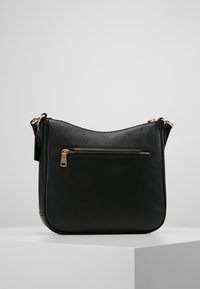 Black pebbled leather shoulder bag with a front zip pocket and gold-tone hardware, placed on a white display pedestal.