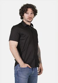 Camicia a maniche corte, con colletto, di tessuto nero uniforme con bottoni sul davanti; abbinata a jeans in denim blu.