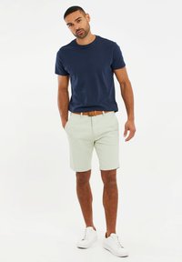 Camiseta de algodón navy, pantalones cortos verde claro, cinturón marrón y zapatillas blancas. Diseño sencillo, mangas cortas y tejido ligero.