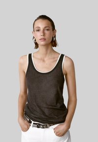 Donkergrijze tanktop met witte contrasterende randen, gemaakt van een zachte stof, met een ontspannen pasvorm en een ronde halslijn. In combinatie met een riem met zilveren accenten.