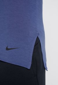Violetti urheilupaitaa, jossa on pyöristetty helma, lyhyet hihat, sivuaukot ja musta Nike-logo vasemmassa alakulmassa.