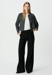 Szara, krótka kurtka z dwoma przednimi kieszeniami, w połączeniu z białą bluzką i czarnymi spodniami o wysokim stanie. Teksturowany materiał i elegancki fason.