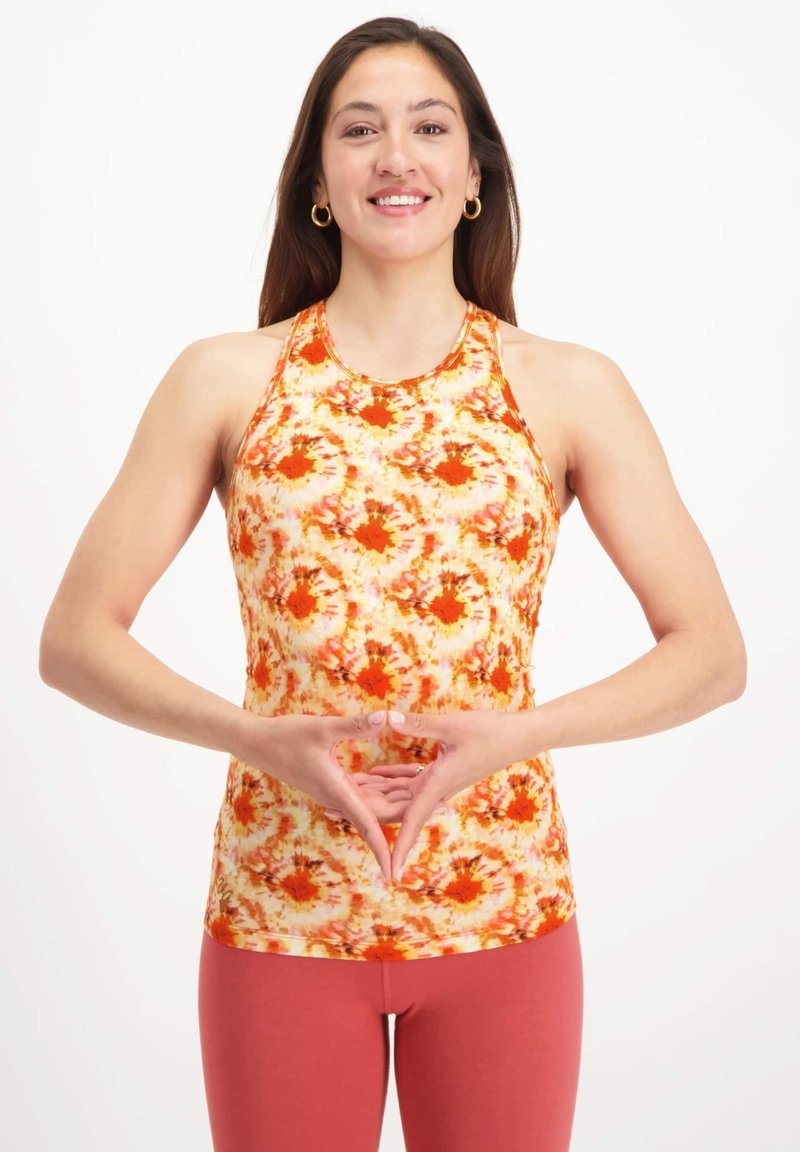 Halter-top i orange och gul batikmönster, tillverkad av stretchigt material, kombinerad med rosa tajta leggings. Anmärkningsvärda designdetaljer inkluderar en hög halsringning.